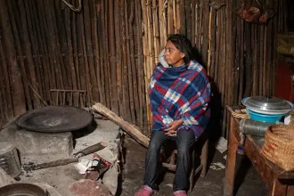 A woman sits next to her wood-burning stove in Mexico