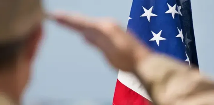 A person in military uniform salutes the American flag